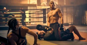 Cena do filme 60 Minutos (2024), com Octavio (interpretado por Emilio Sakraya) em um ringue de luta, exibindo físico imponente e luvas de boxe, enquanto encara o adversário dominado no chão — destaque para a intensidade das artes marciais no thriller de ação alemão da Netflix.