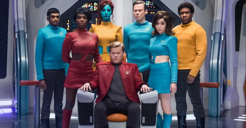 Cena do episódio USS Callister da série Black Mirror (2011–atualmente), com Robert Daly (Jesse Plemons) ao centro, rodeado por sua tripulação digital: Nanette Cole (Cristin Milioti), Shania Lowry (Michaela Coel), Kabir Dudani (Paul G. Raymond), Walton (Jimmi Simpson), Elena (Milanka Brooks) e Nate Packer (Osy Ikhile), em uma paródia sombria de ficção científica inspirada em Star Trek.