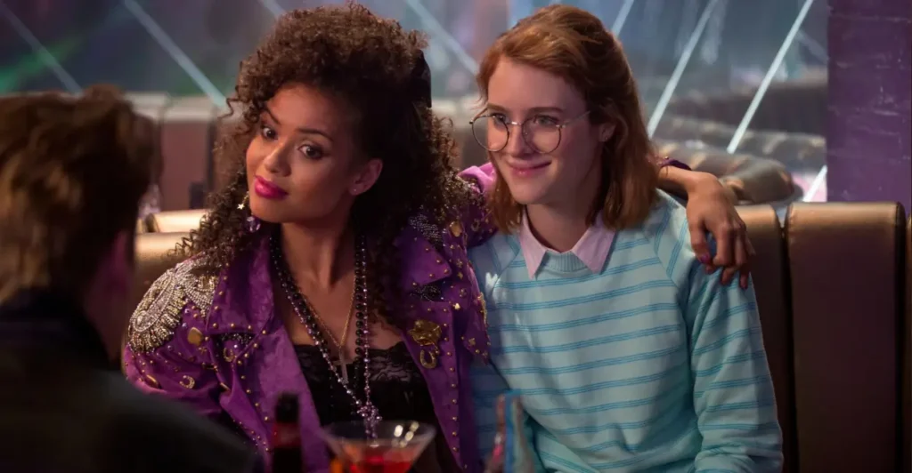 Cena do episódio San Junipero da série Black Mirror (2011–atualmente), com Yorkie (Mackenzie Davis) e Kelly (Gugu Mbatha-Raw) em clima de romance em uma boate dos anos 1980 — destaque para a atmosfera nostálgica e emocional de um dos episódios mais aclamados da antologia futurista da Netflix.