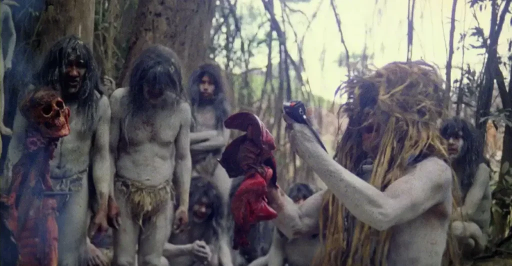 Cena perturbadora do filme Holocausto Canibal mostrando tribo fictícia na floresta realizando ritual com órgãos humanos e pintura corporal, símbolo do terror extremo dos anos 1980.