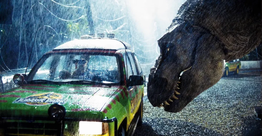 Cena clássica de Jurassic Park (1993) com o Tiranossauro Rex encarando um dos carros turísticos do parque sob forte chuva, simbolizando tensão e avanço dos efeitos especiais no cinema.