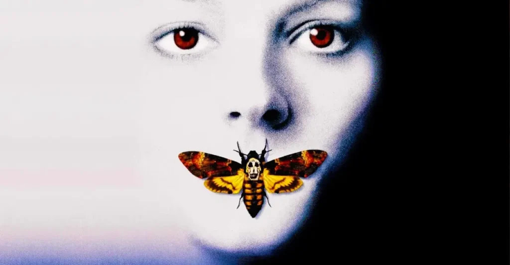 Pôster icônico de O Silêncio dos Inocentes, com rosto feminino pálido de olhos vermelhos e uma mariposa com crânio nas asas cobrindo a boca, simbolizando o silêncio e o terror psicológico do filme.