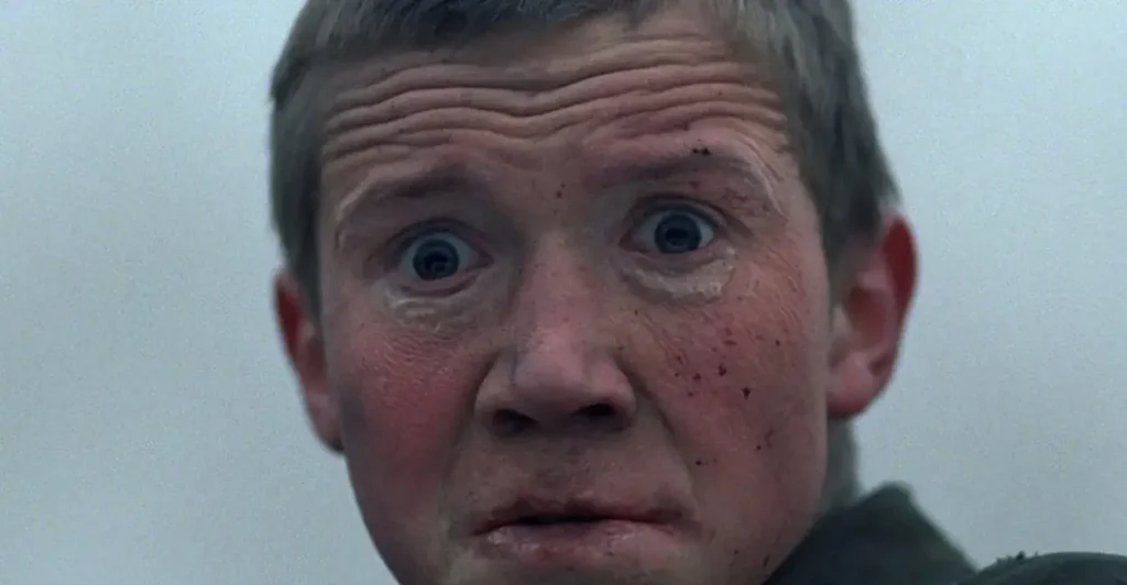 Close impactante do filme Vá e Veja (1985), mostrando o personagem Florya Gaishun (interpretado por Aleksei Kravchenko) com expressão de horror e desespero, simbolizando o trauma psicológico e a brutalidade da guerra vivida pelo protagonista no clássico soviético de Elem Klimov.