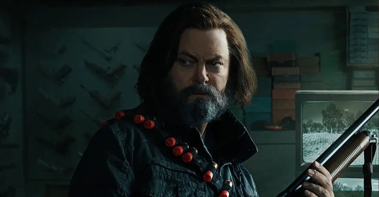 Bill, personagem de The Last of Us, empunha espingarda com cartucheira de munição no ombro, em cena tensa dentro de seu refúgio fortificado.