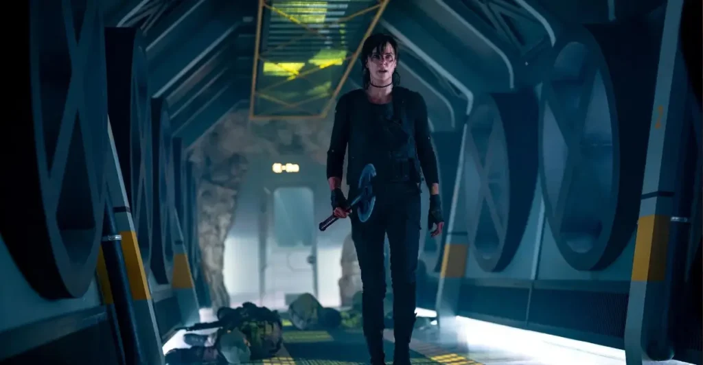 Personagem de The Old Guard 2 (2025) caminha por corredor futurista com machado em mãos, após confronto, em cena de ação intensa.
